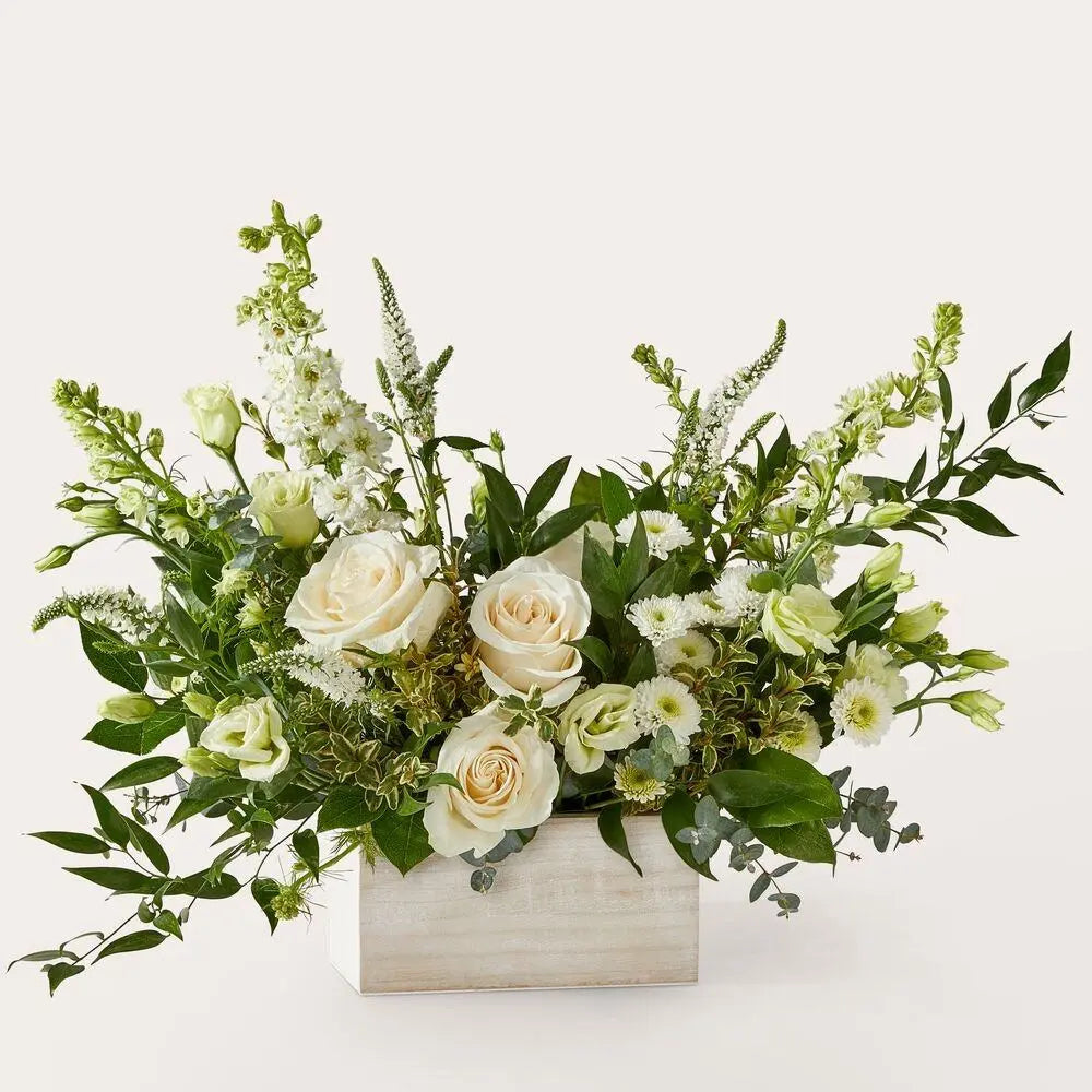 Floral arrangement with white and green flowers in a pale wooden box on a light background